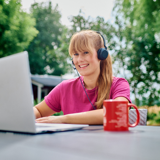 Frau mit Headset arbeitet im Homeoffice im Freien am Laptop.