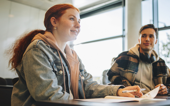 Eine junge Frau sitzt gemeinsam mit einem Klassenkameraden in einem Schulungsraum