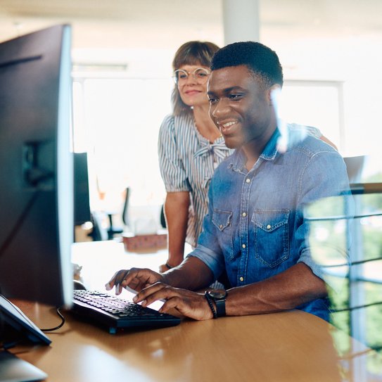Zwei Mitarbeitende blicken auf einen PC-Monitor.