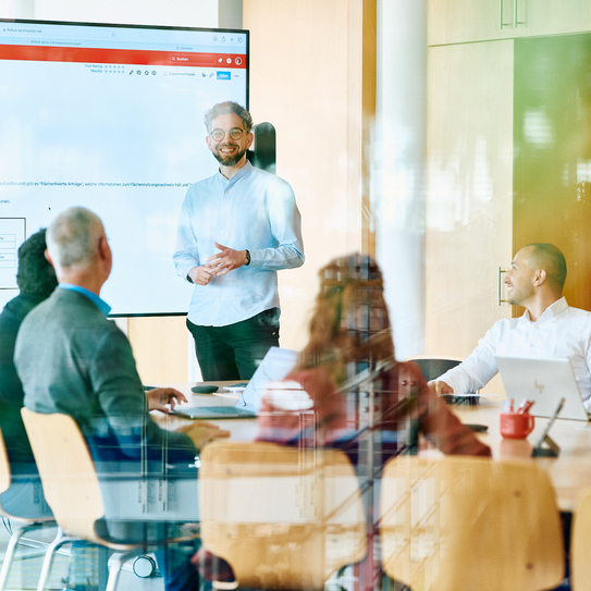 Mitarbeitende befinden sich in einer Schulung, ein Mann steht vor sitzenden Menschen und erzählt.