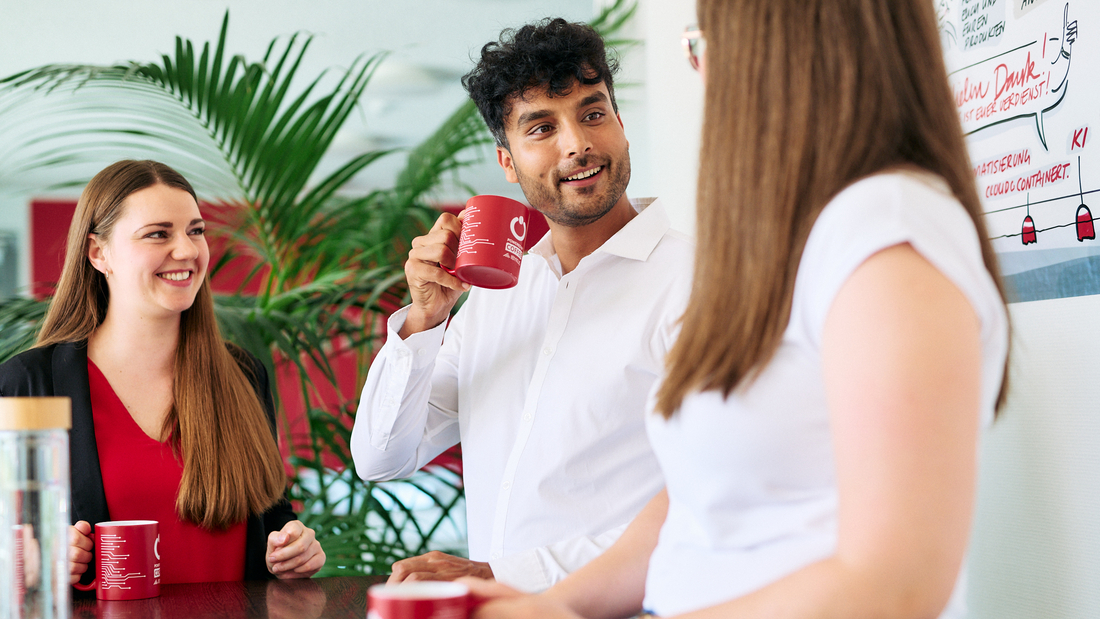 Drei Kolleg:innen stehen in ihrer Kaffeepause zusammen an einem Stehtisch und unterhalten sich.