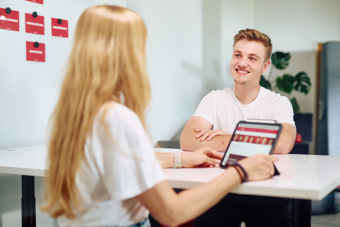 Ein Gespräch zwischen einer Frau und einem jungen Mann. An der Wand hinter den beiden hängen die Werte der IBYKUS Ag als Postkarten.