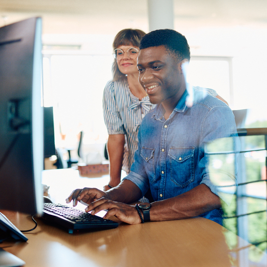 Eine Mitarbeiterin zeigt einem Mitarbeiter etwas am Computer