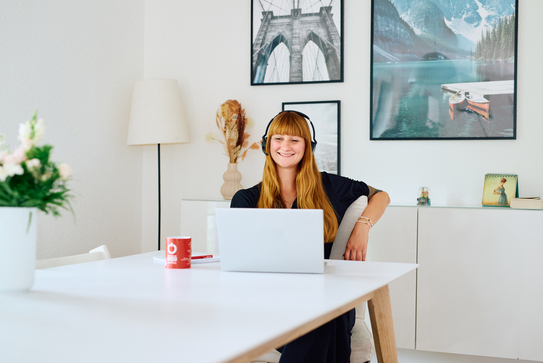 Eine Frau mit langen roten Haaren sitzt in ihrem Wohnzimmer am Laptop