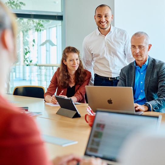 Drei Personen in einem modernen Büro bei einer gemeinsamen Besprechung am Laptop.